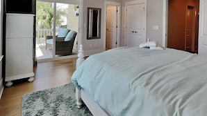 A bedroom with a large bed, a ceiling fan, a sliding glass door to a balcony, and a white wardrobe. - Serenity By the Sea by Carolina Retreats (Kure Beach)
