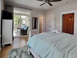 Quarto com uma cama grande, ventoinha no teto, porta de vidro deslizante para uma varanda e um guarda-roupa branco.