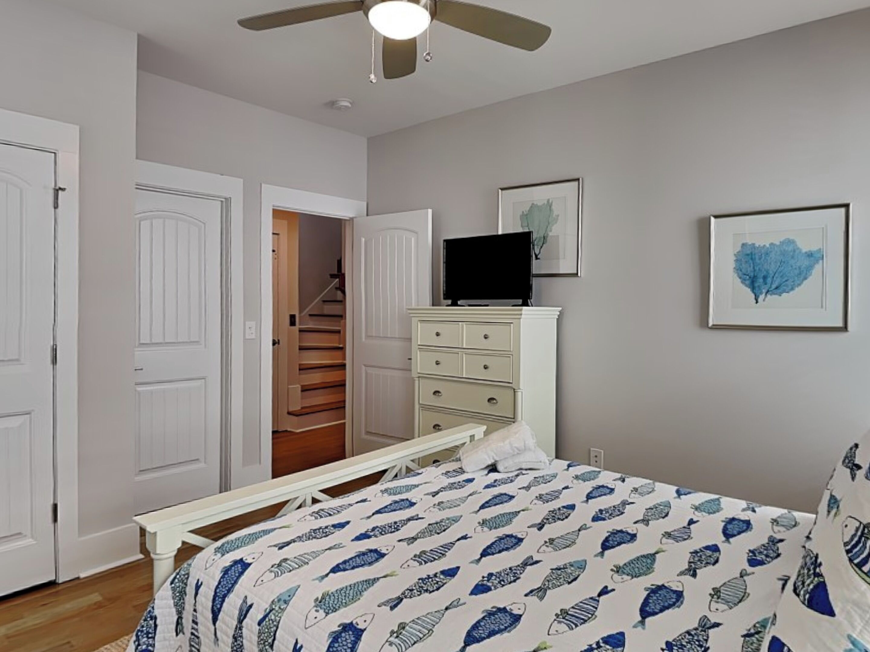 A bedroom with a bed, a dresser, a television on top, and a staircase leading to a closet.