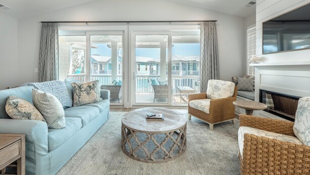 A spacious living room with a light blue sofa, wicker armchairs, a round coffee table, and a fireplace. - Serenity By the Sea by Carolina Retreats (Kure Beach)