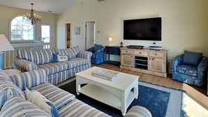 A living room with striped sofas, a coffee table, a TV, and a wooden cabinet. - Summer Wynd by Topsail Realty (Sneads Ferry)