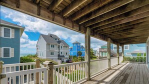 A covered wooden deck with a white railing, overlooking a residential area with blue and gray houses. - Summer Wynd by Topsail Realty (Sneads Ferry)