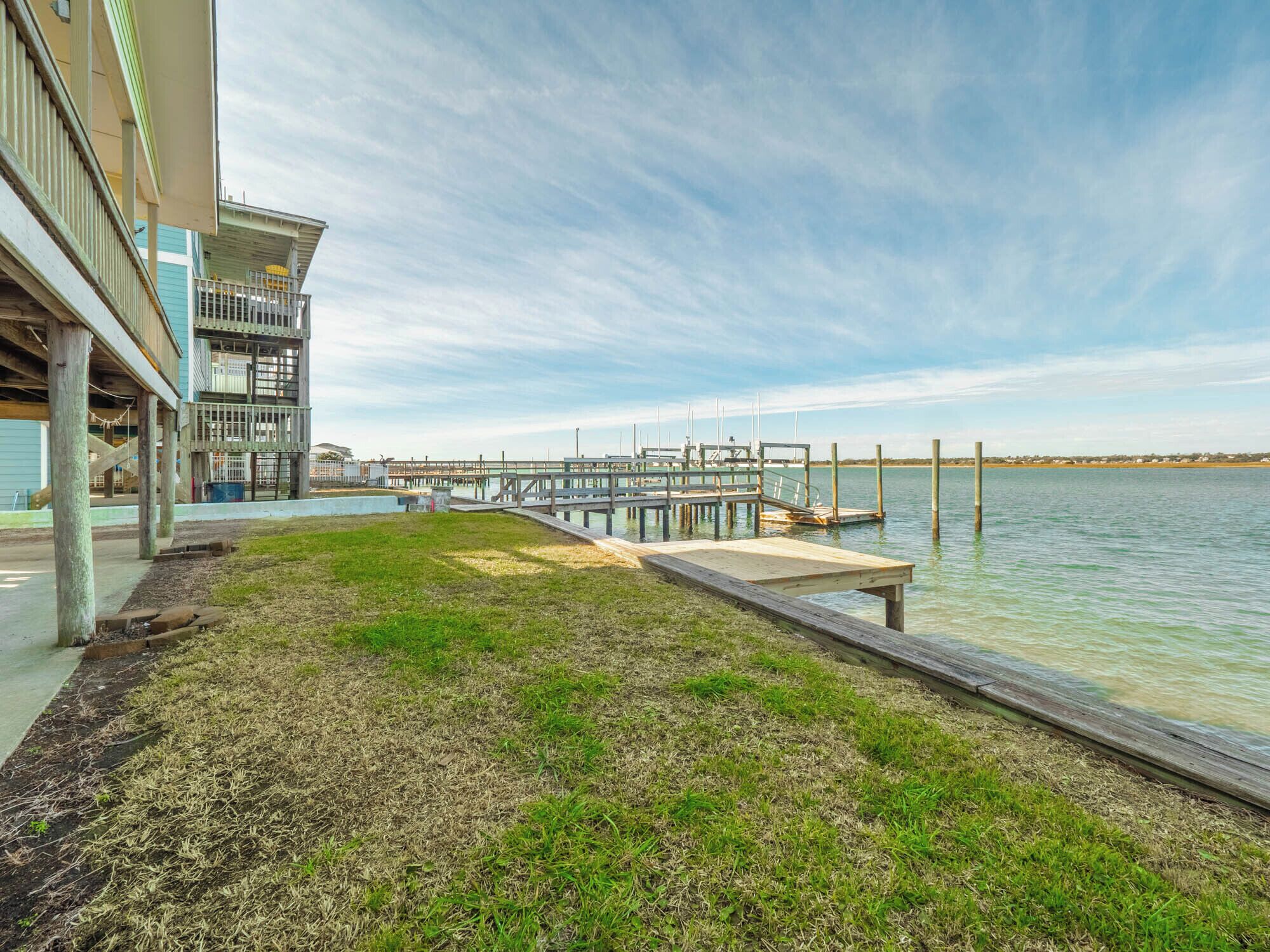 A waterfront property with a dock extending into the water, a grassy area, and a building with a balcony.