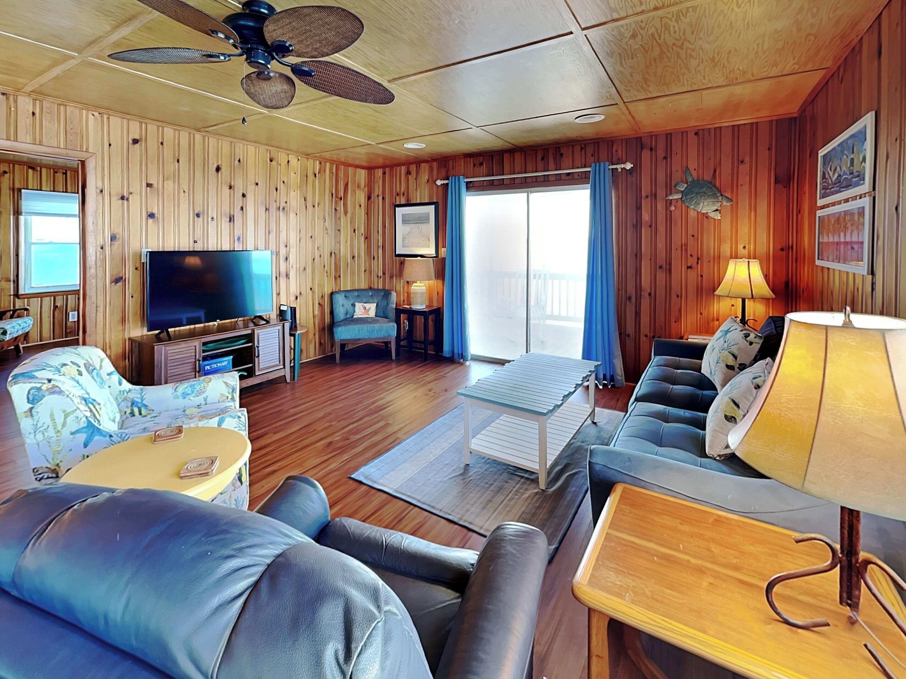 Un intérieur de chalet chaleureux avec des murs en bois, un ventilateur de plafond, un téléviseur à écran plat, un canapé, une table basse et une lampe.