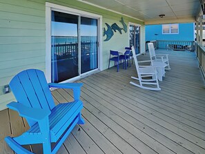 A wooden deck with blue and white Adirondack chairs, a glass door leading to a balcony, and a blue building with a fish mural.