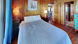 A wooden-paneled room with a large bed, two bedside tables with lamps, a dresser, and a painting on the wall. - Seahorse Sound by Topsail Realty (Holly Ridge)