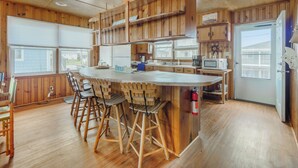 A kitchen with wooden cabinets, a central island with stools, a microwave, and a refrigerator. - Seahorse Sound by Topsail Realty (Holly Ridge)