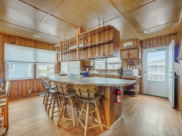 A kitchen with wooden cabinets, a central island with stools, a microwave, and a refrigerator. - Seahorse Sound by Topsail Realty (Holly Ridge)