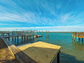A wooden dock extending into calm waters with a clear sky above.