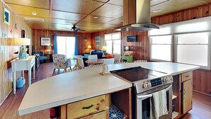 A kitchen with a central island, wooden cabinets, and a stainless steel stove. - Seahorse Sound by Topsail Realty (Holly Ridge)