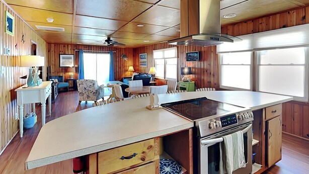 Een keuken met een centraal eiland, houten kastjes en een roestvrijstalen fornuis.