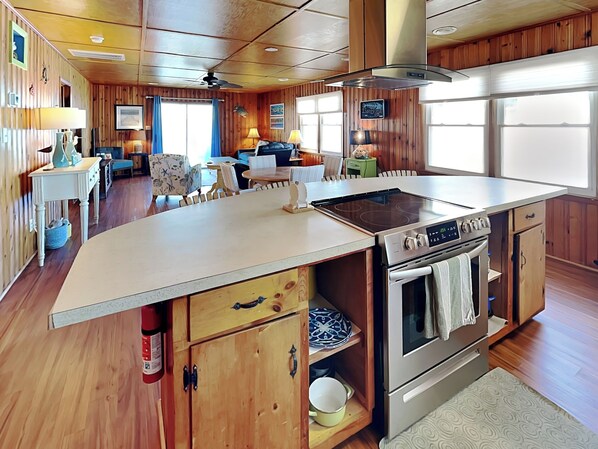 A kitchen with a central island, wooden cabinets, and a stainless steel stove. - Seahorse Sound by Topsail Realty (Holly Ridge)