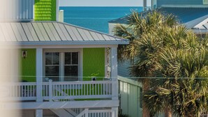 A coastal house with a green facade, white balcony, and a view of the ocean. - Love Kure by Carolina Retreats (Kure Beach)
