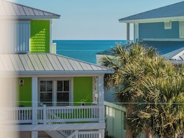 Uma casa costeira com fachada verde, varanda branca e vista para o mar.