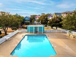 Uma piscina com cerca branca, um pequeno coreto e casas coloridas ao fundo.