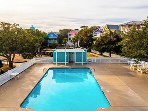 Piscina com um deck branco, cercada por uma cerca e árvores.