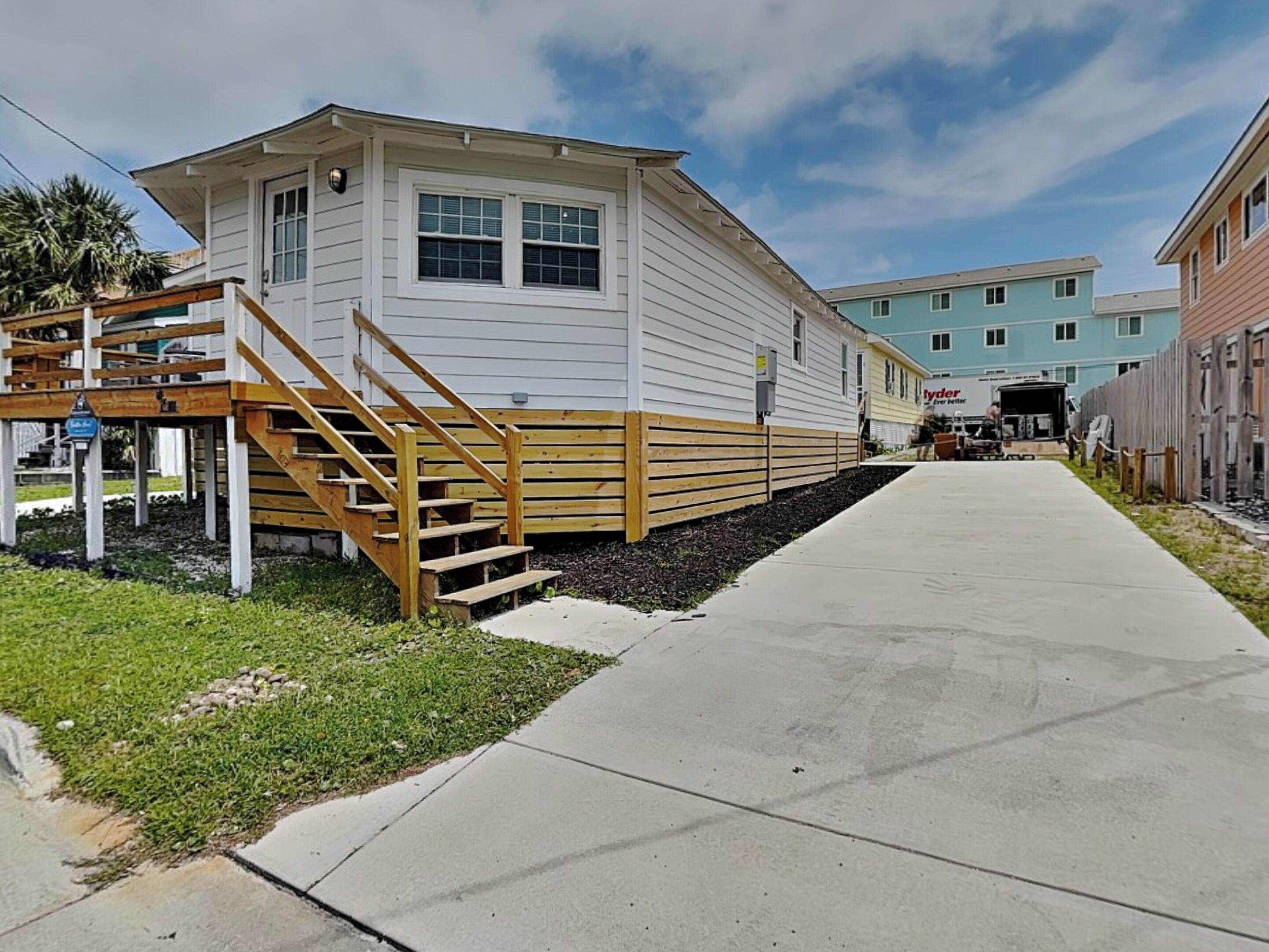 A two-story building with a wooden staircase leading to a deck, a concrete pathway, and a clear sky.