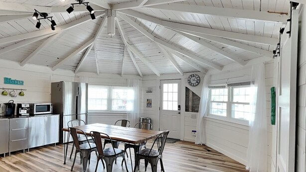 A spacious kitchen with a wooden table and chairs, a refrigerator, and a clock on the wall. - Toes in the Sand by Carolina Retreats (Carolina Beach)