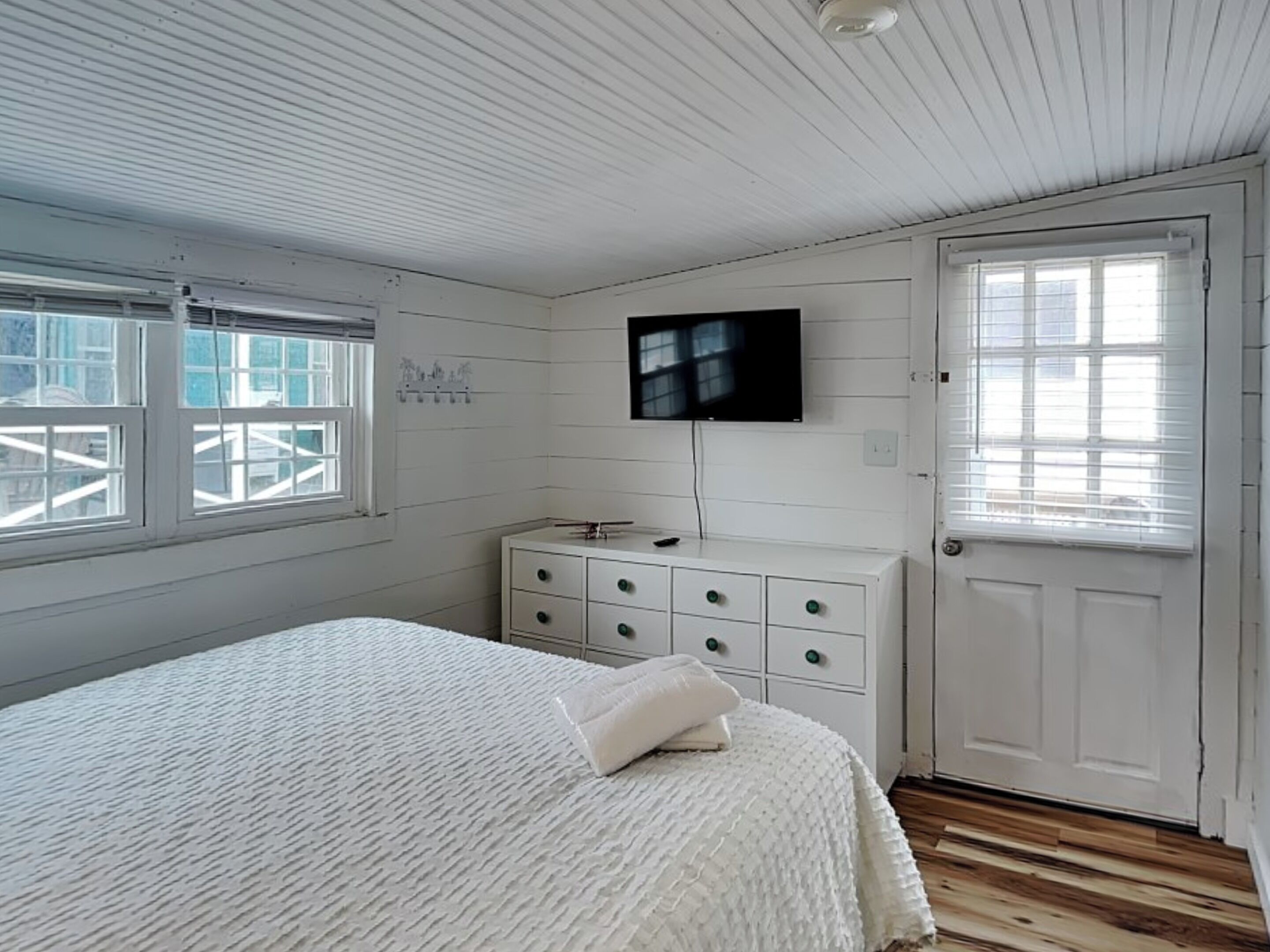 A bedroom with a bed, a dresser, a television, and a door.