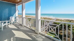 A covered outdoor area with a view of the beach, white chairs, and a wooden ceiling. - Blue Oyster by Carolina Retreats (Carolina Beach)