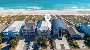 An aerial view of a beachfront hotel with multiple buildings, a beach in the background, and a clear sky. - Blue Oyster by Carolina Retreats (Carolina Beach)