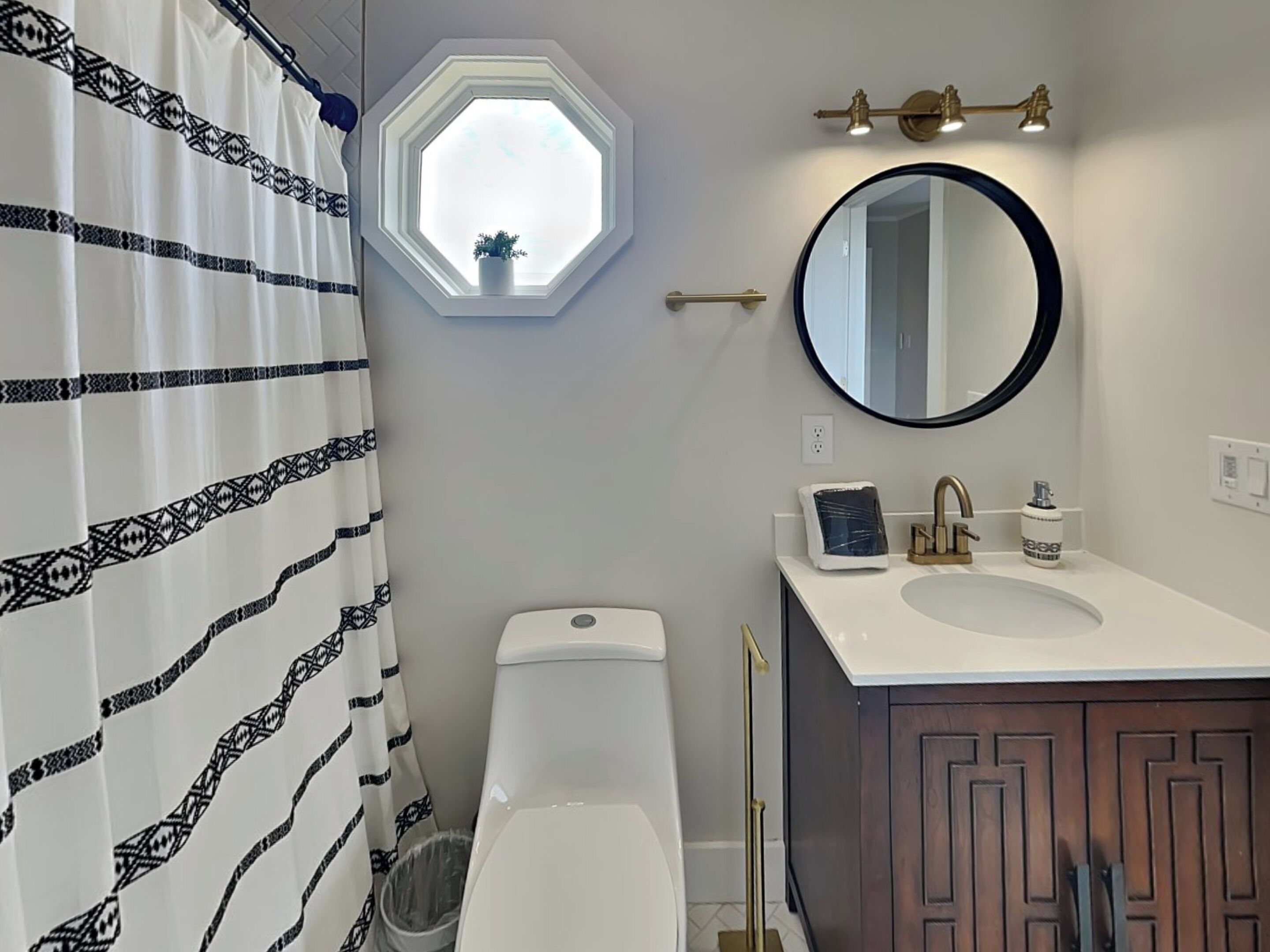 A bathroom with a white toilet, a sink with a mirror, a shower curtain, and a window with a plant.