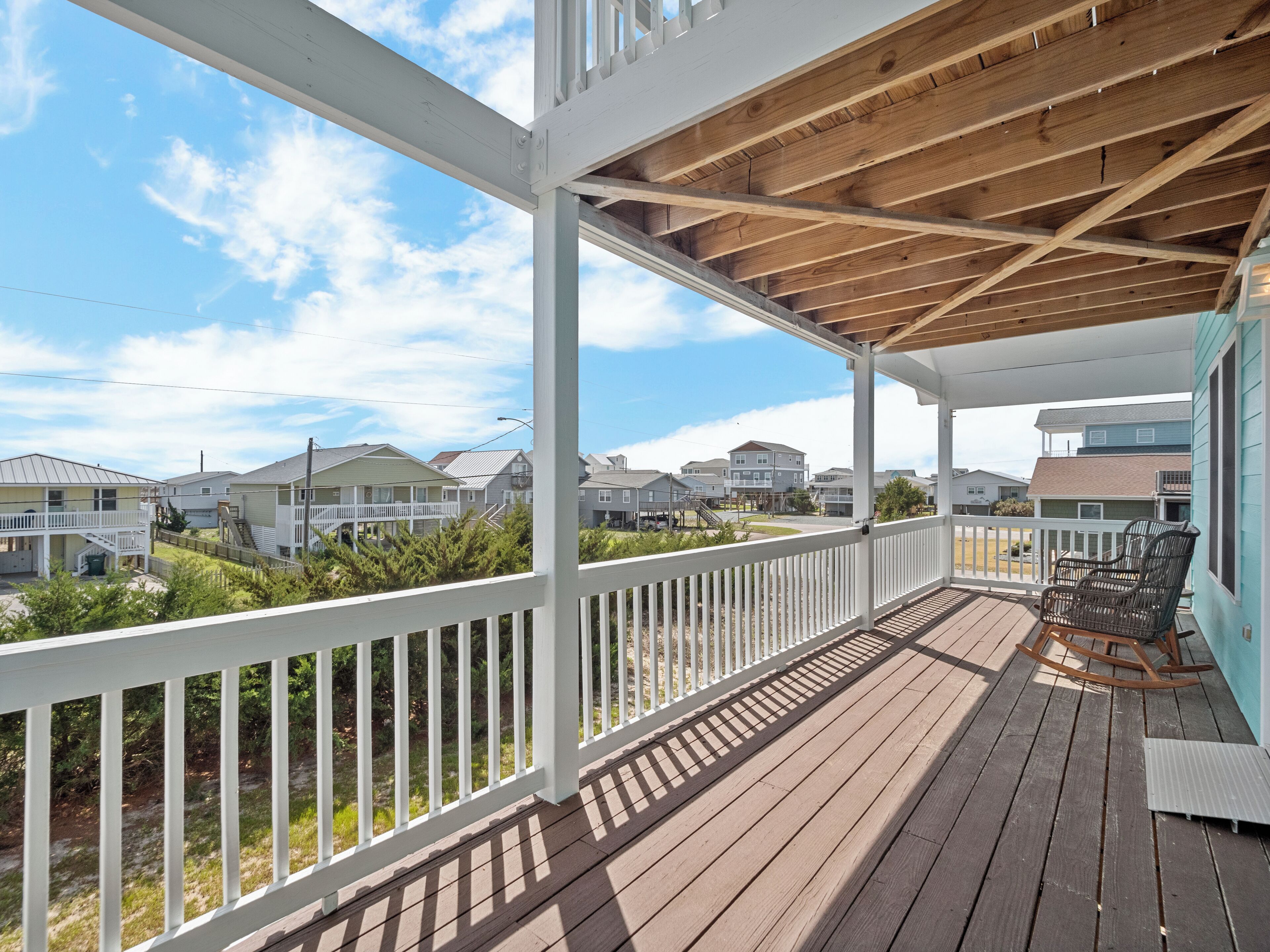 A wooden deck with white railings, a covered area, and a view of neighboring houses.