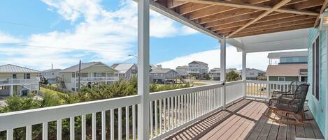 A wooden deck with white railings, a covered area, and a view of neighboring houses.