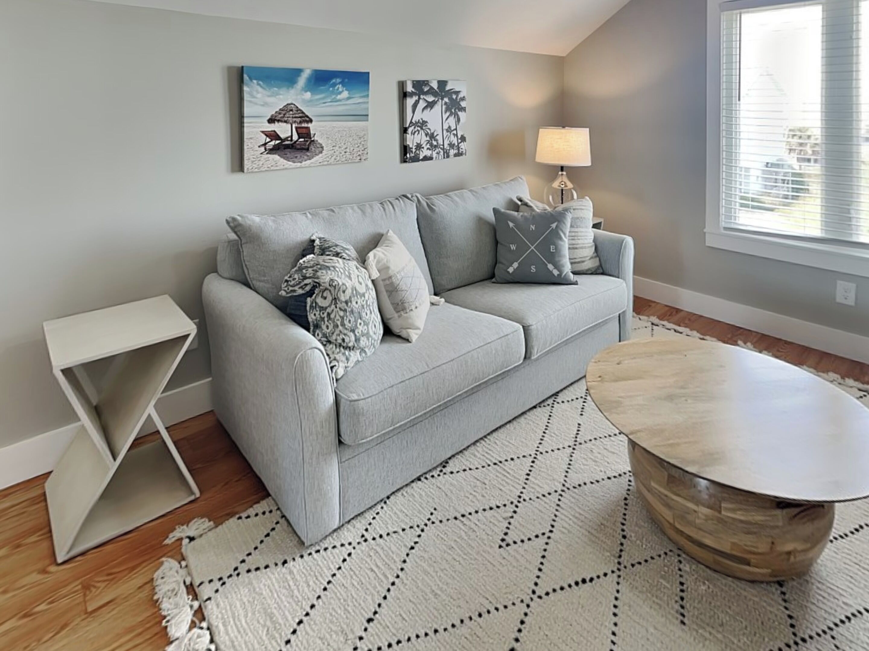 A modern living room with a grey sofa, a round wooden coffee table, and a patterned rug.