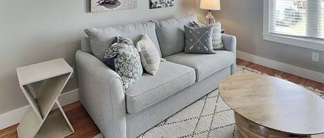 A modern living room with a grey sofa, a round wooden coffee table, and a patterned rug.