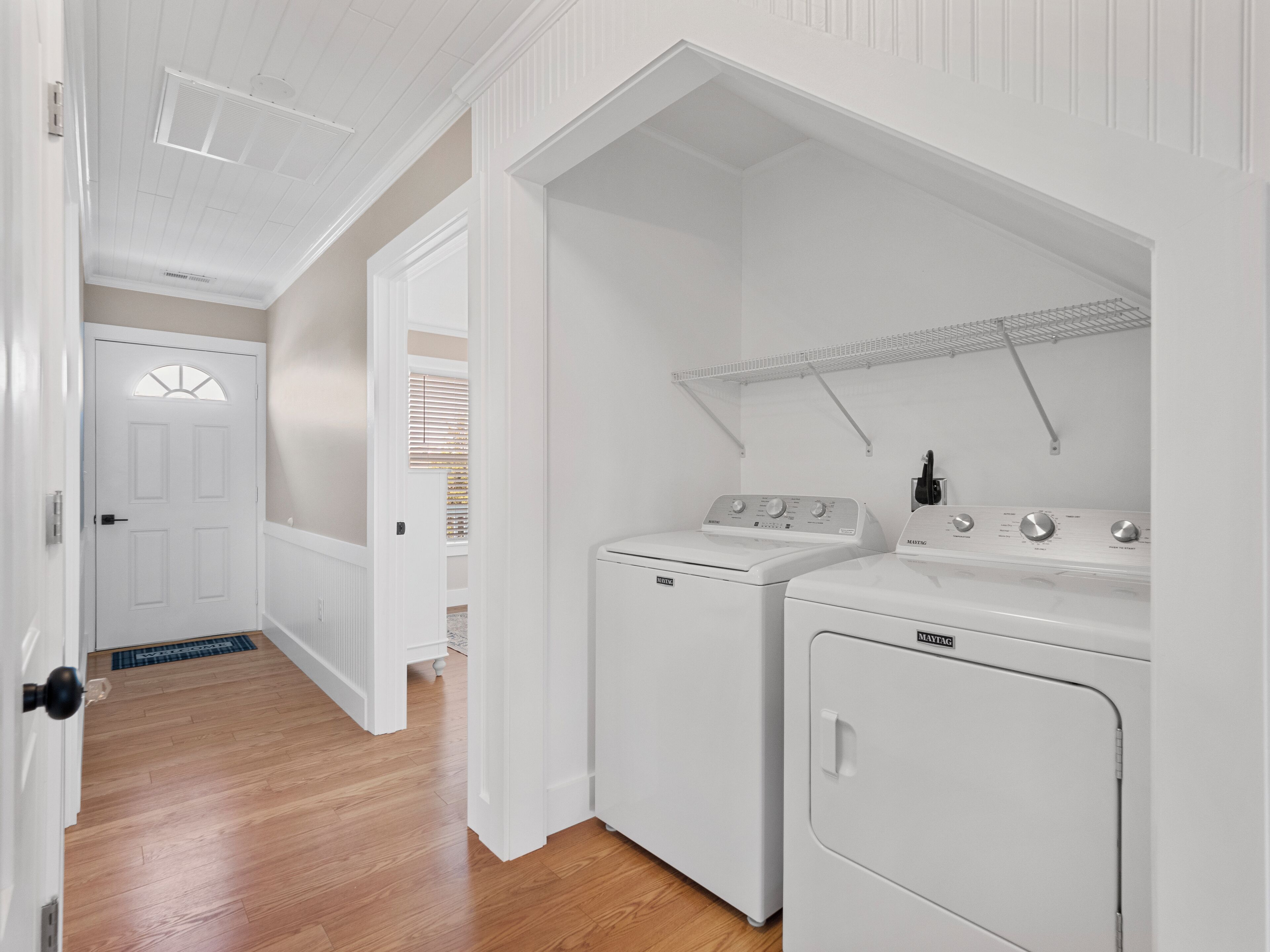 Un cuarto de lavandería con lavadora y secadora, piso de madera y una puerta blanca con ventana.