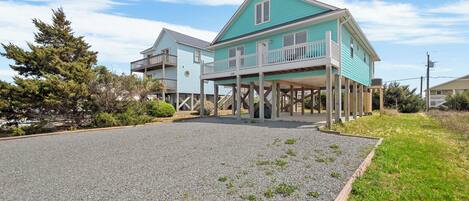 A two-story house with a balcony, wooden deck, and a gravel driveway.