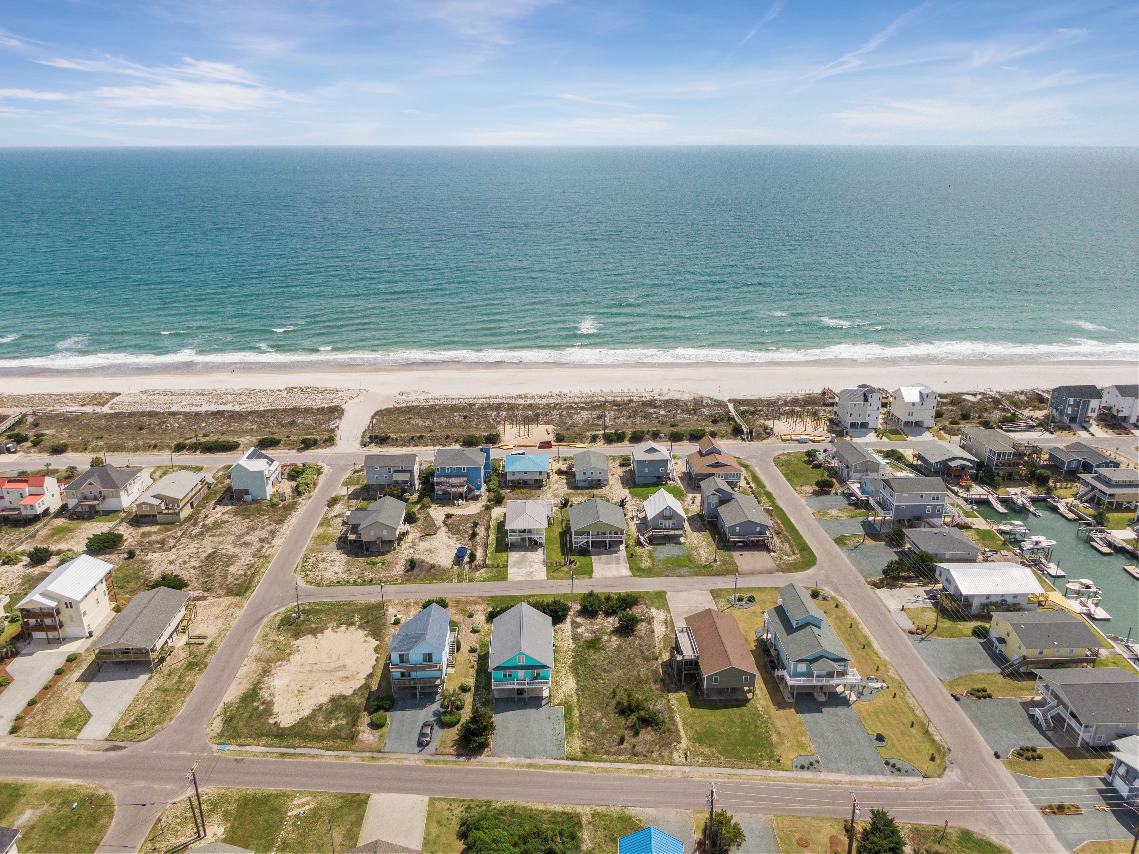 An aerial view of a coastal residential area with houses, a marina, and a beach.