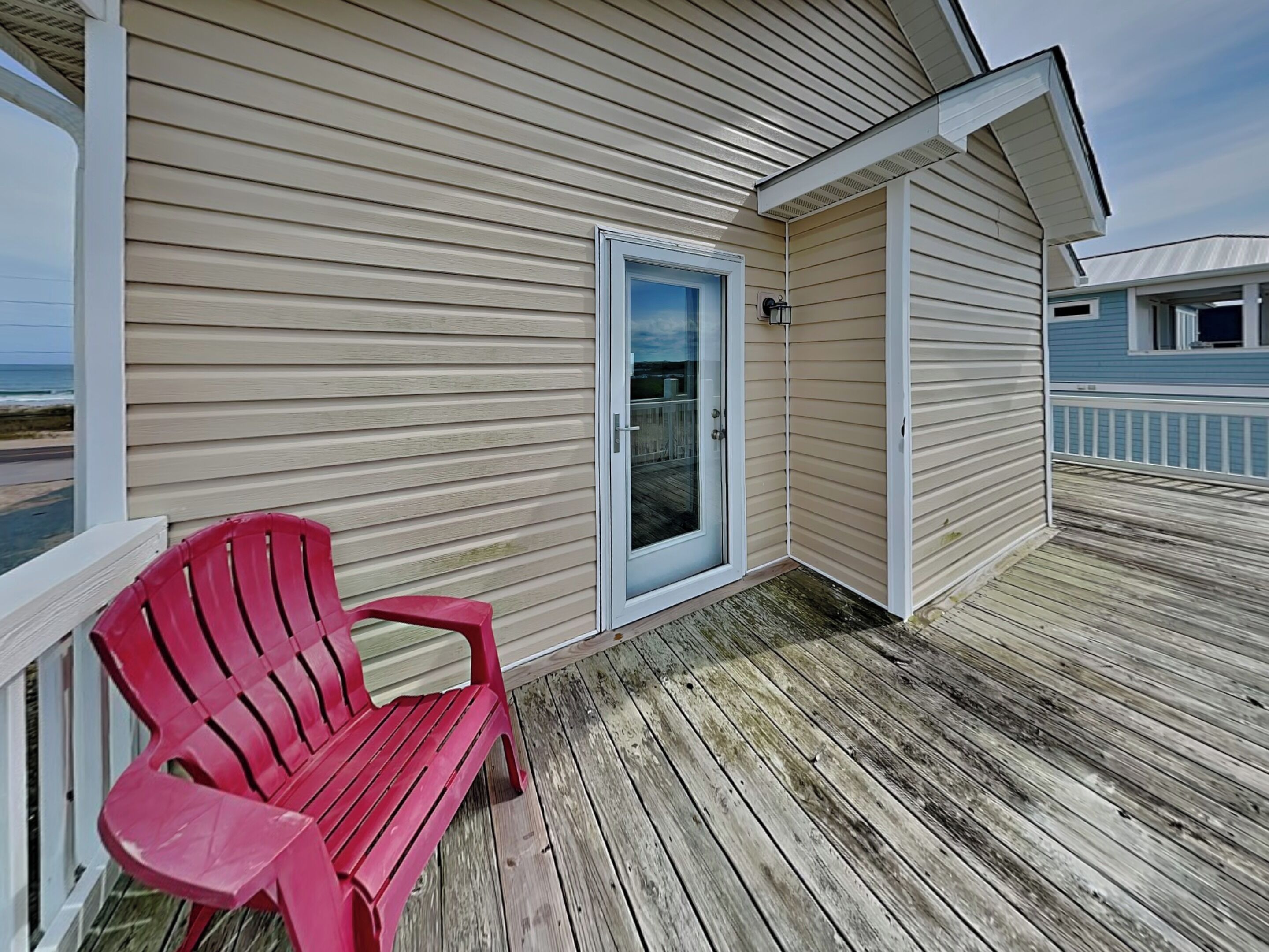 A wooden deck with a red chair, a door, and a view of the ocean.