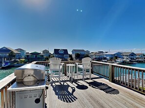 Eine Holzterrasse mit Grill und Stühlen mit Blick auf eine Marina und Häuser.