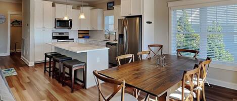A modern kitchen with white cabinetry, a central island, and a dining area with wooden chairs.
