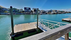 A wooden dock extending into calm water with houses in the background. - Sunset Nonsense by Topsail Realty (Holly Ridge)