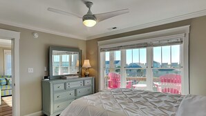 A bedroom with a bed, dresser, and a ceiling fan. There is a window with blinds and a view of the outside. - Sunset Nonsense by Topsail Realty (Holly Ridge)