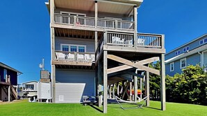 A two-story building with a balcony on the upper floor, a garage at the base, and a playground structure in front. - Sunset Nonsense by Topsail Realty (Holly Ridge)