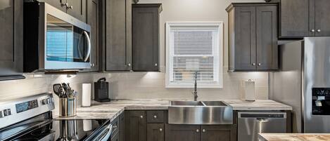 A modern kitchen with dark cabinetry, stainless steel appliances, and a large window.