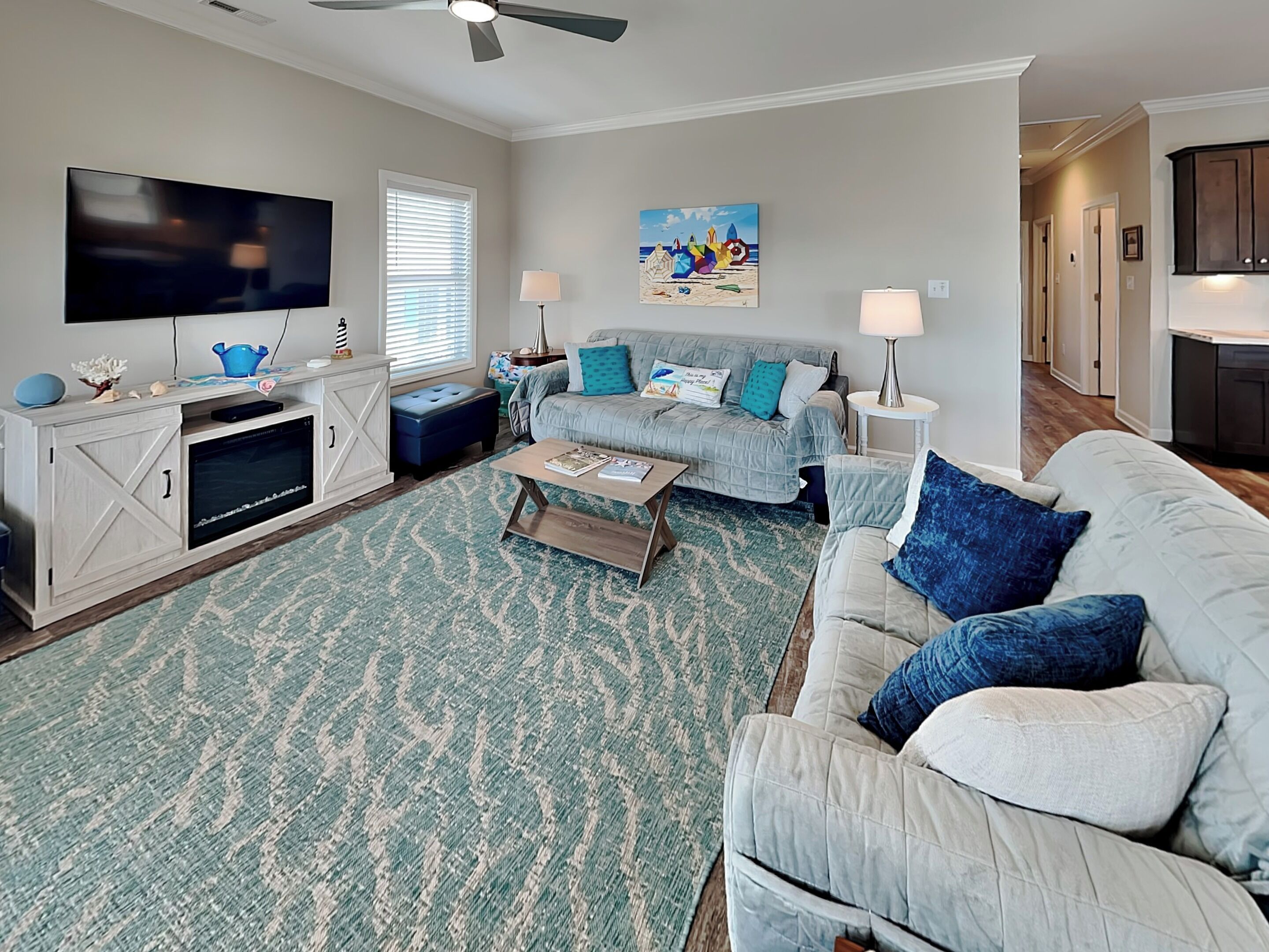 A living room with a large flat-screen TV, a sofa, a coffee table, and a patterned rug.