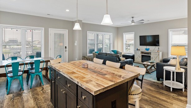 A spacious living area with a wooden island, a dining table with chairs, a sofa, a TV, and a ceiling fan.