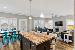 A spacious living area with a wooden island, a dining table with chairs, a sofa, a TV, and a ceiling fan.
