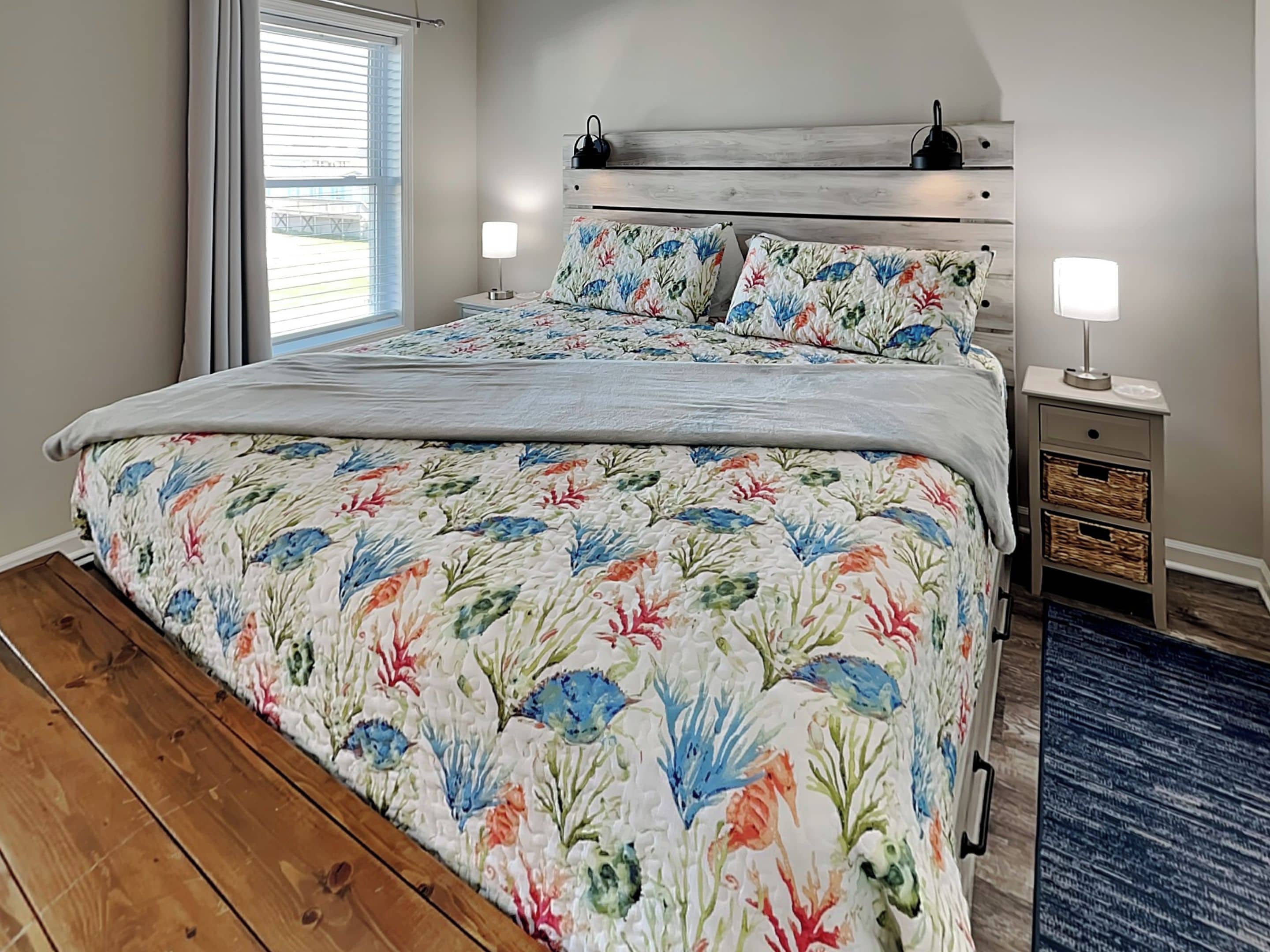 A bedroom with a bed, two bedside tables, a nightstand, a window with blinds, and a blue rug.
