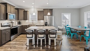 A modern kitchen with dark wood cabinets, a stainless steel refrigerator, a built-in microwave, and a large island with bar stools.