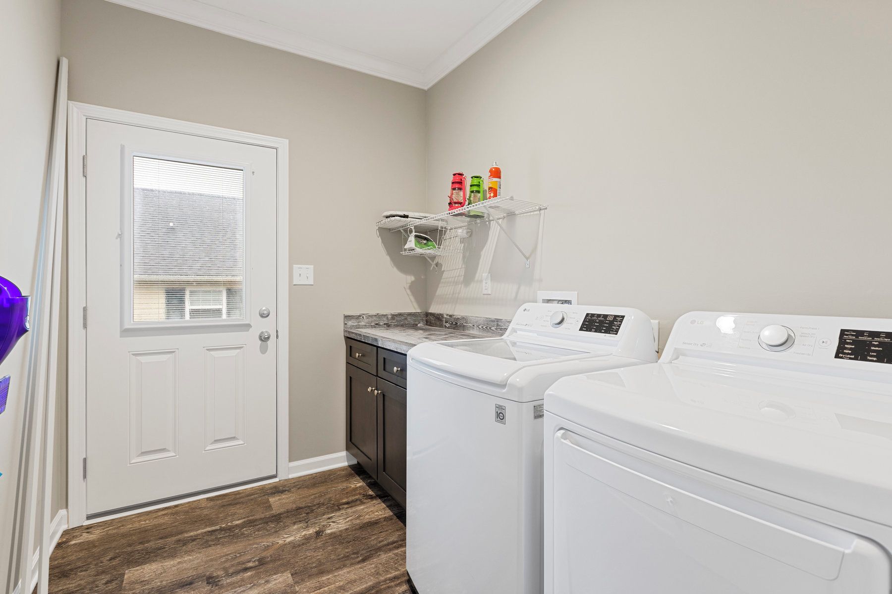 A laundry room with two white front-loading washers and dryers, a wooden cabinet, and a shelf with laundry supplies.