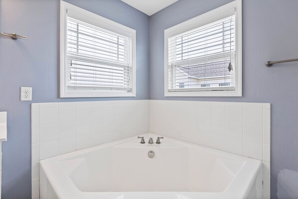 A corner bathroom with a bathtub, two windows with blinds, and a towel rack. - Palm Beach North by Topsail Realty (Sneads Ferry)