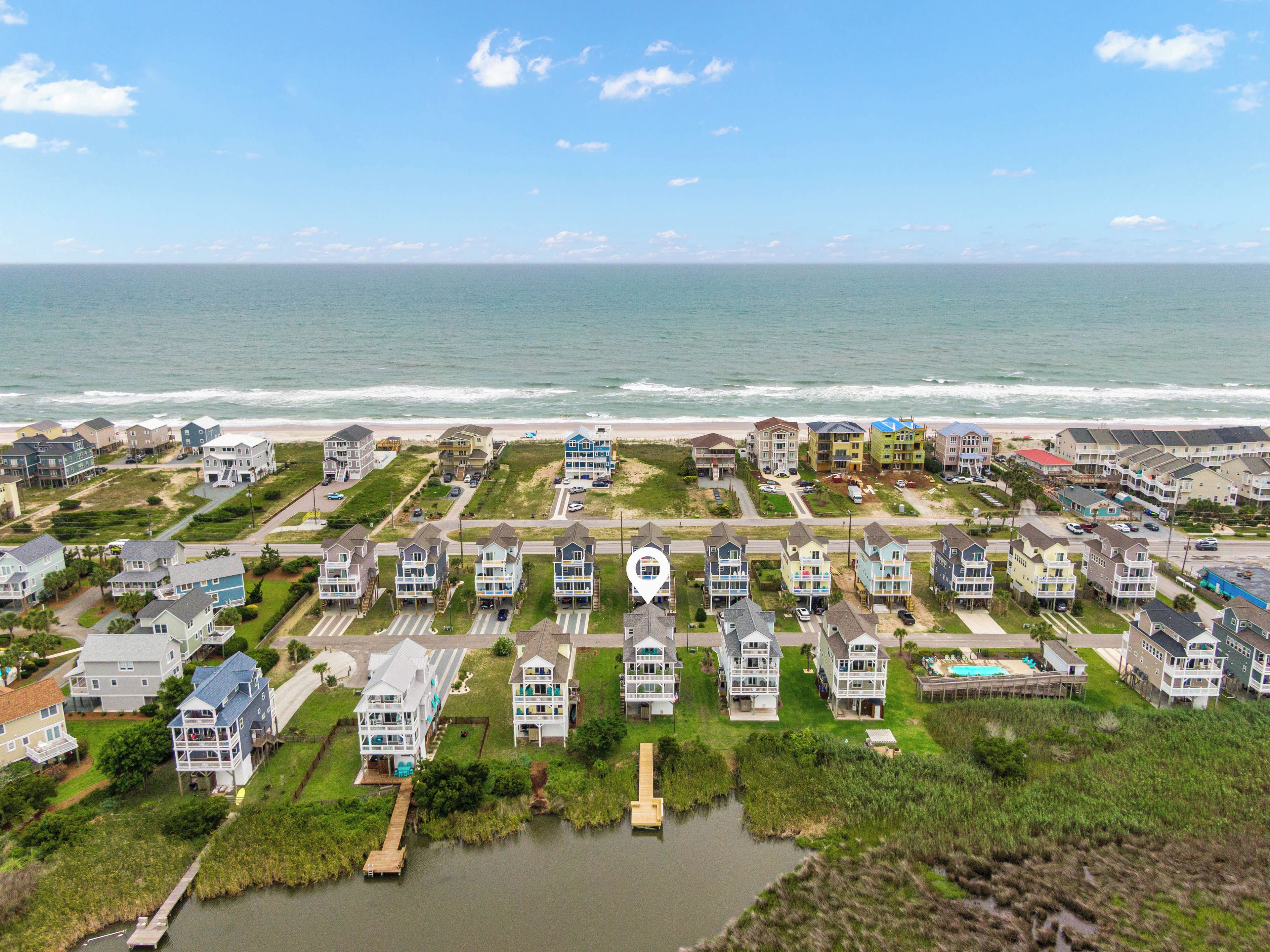 A coastal residential area with houses near the beach, a small water body, and a clear sky.