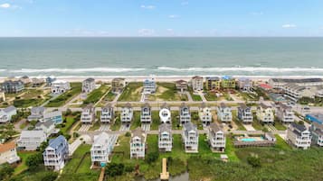 A coastal residential area with houses near the beach, a small water body, and a clear sky.