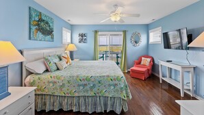 A bedroom with a bed, a ceiling fan, a TV, and a window with a view. - Palm Beach North by Topsail Realty (Sneads Ferry)